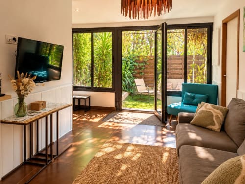 Séjour lumineux avec vue sur le jardin, fauteuil bleu-vert, télévision écran plat et accès direct à la terrasse à Maison D'hôtes Coeur