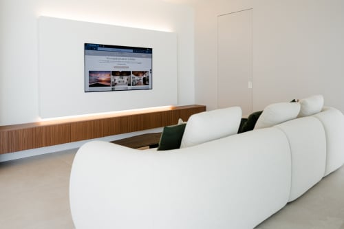 Sala moderna en villa Alisio de V&C en VC Luxury Village con sofá curvo blanco, panel de madera y TV empotrada