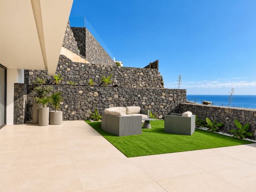 Terraza de la villa Alisio V&C con vistas al mar, muros de piedra, tumbonas, césped artificial y plantas en macetas en VC Luxury Village