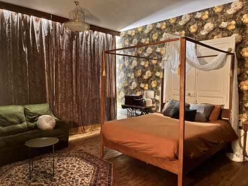 Chambre luxueuse avec lit à baldaquin en bois, literie orange, papier peint fleuri et canapé vert aux Studios Chez Mary à Gannat