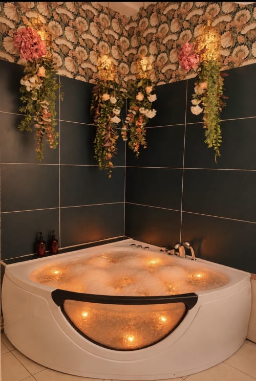 Luxueux jacuzzi d'angle avec éclairage chaleureux et décors floraux en cascade aux Studios Chez Mary Gannat
