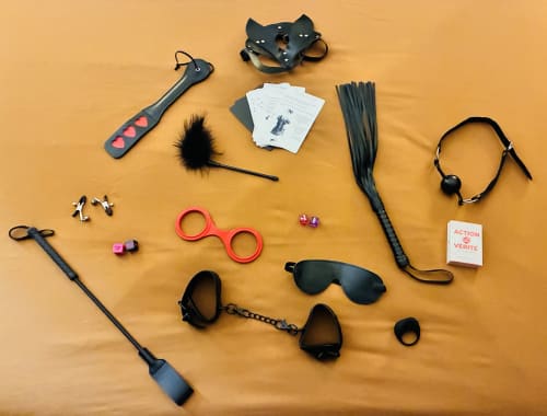 Collection d'accessoires pour l'intimité des adultes présentée sur fond orange pour Chez Mary Studios Gannat