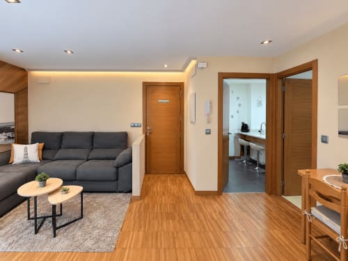 Moderno salón de apartamento en Baiona con sofá oscuro, suelos de madera y vistas a la ciudad