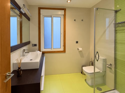 Baño moderno en apartamento Aire de Baiona con suelo verde lima, detalles de madera y ducha abierta