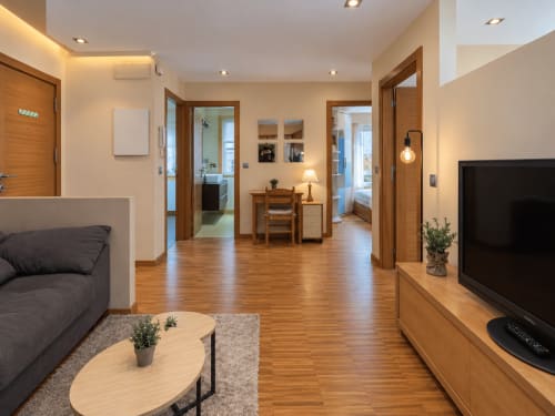 Salón moderno en Baiona con suelos de madera, TV, sofá y distribución abierta hacia dormitorio y baño
