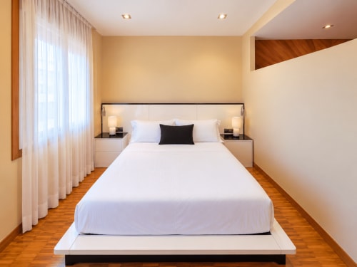 Dormitorio moderno en apartamento Aire de Baiona con cama blanca, pisos de madera y vistas a la ciudad