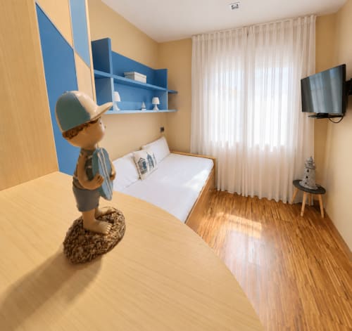 Dormitorio de apartamento con temática náutica en Baiona: cama blanca, suelos de madera, TV y faro decorativo con acentos azules