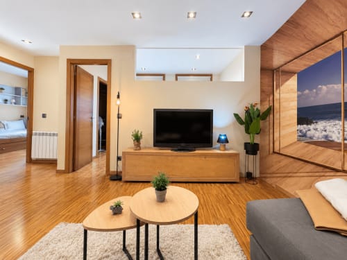 Sala de estar moderna en Baiona con suelos de madera, televisor, plantas y vistas al océano a través de puertas de cristal