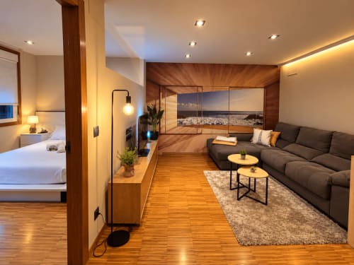 Moderno estudio en Baiona con suelos de madera, sofá oscuro, zona de dormitorio y cuadros con vistas al océano