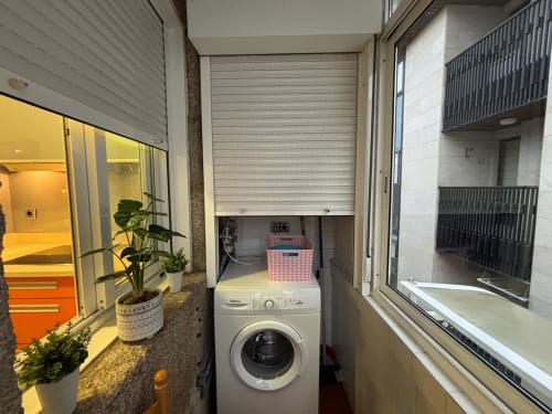 Área de lavandería compacta en apartamento de Baiona con lavadora y estanterías de almacenamiento
