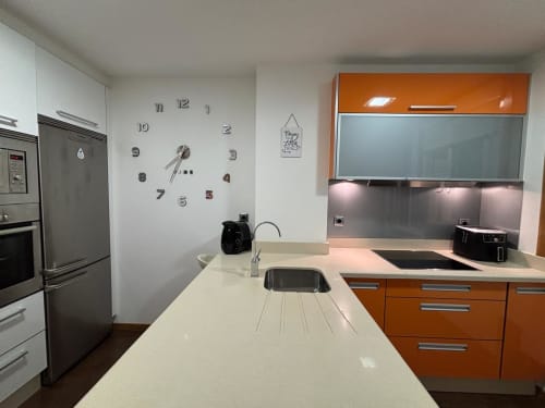Cocina moderna en apartamento de Baiona con muebles naranjas, electrodomésticos de acero inoxidable y encimera blanca