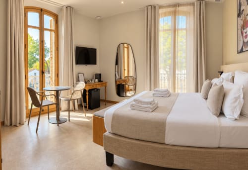 Chambre supérieure élégante au Palmier Aigues-Mortes : lit arrondi, bureau en bois, portes-fenêtres et équipements modernes
