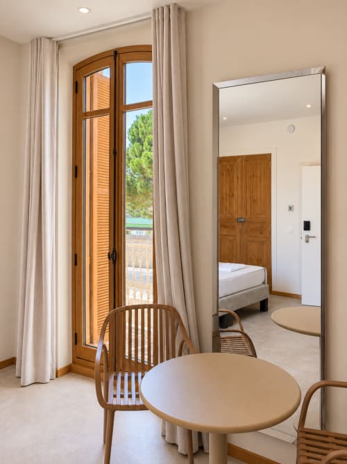 Chambre supérieure au Le Palmier Aigues-Mortes avec table ronde, chaises en bois, accès balcon et miroir reflétant la chambre
