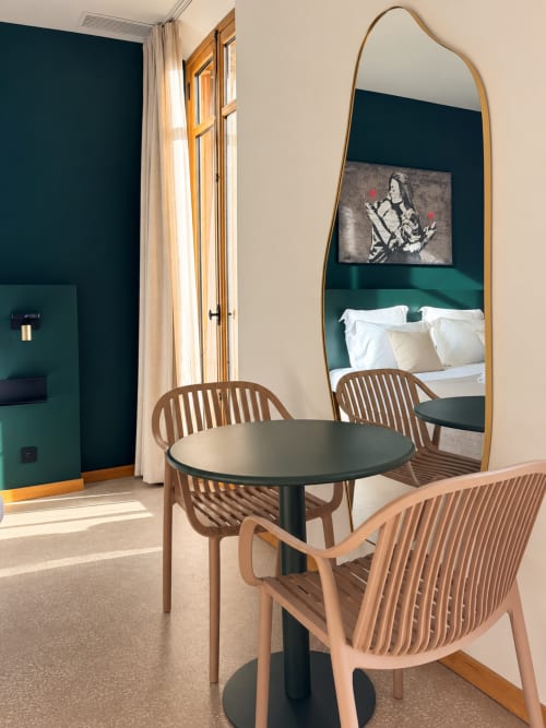 Chambre moderne de l'hôtel Le Palmier Aigues-Mortes avec chaises en bois, table noire, miroir bombé et mur d'accent bleu-vert