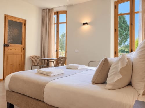 Chambre Standard lumineuse au Palmier Aigues-Mortes avec lit queen, fenêtres en bois, fauteuils et vue sur la campagne
