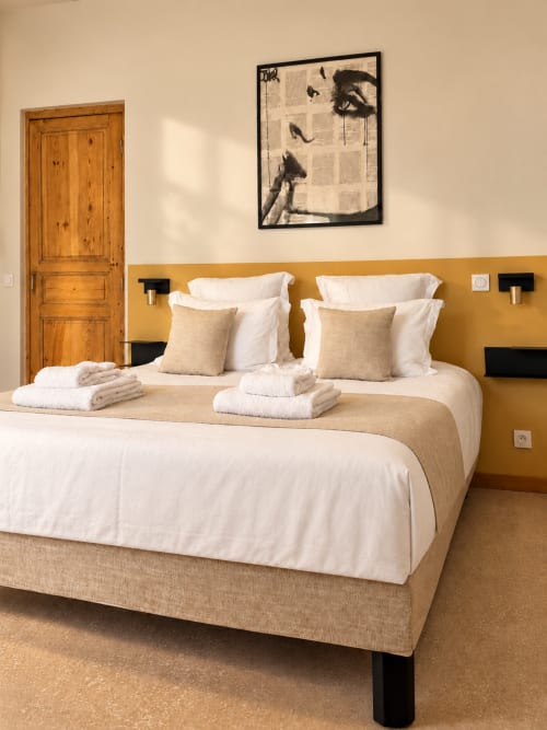 Chambre d'hôtel moderne au Palmier Aigues-Mortes avec lit beige, draps blancs, porte en bois et art mural contemporain
