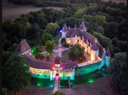Château Hôtel les Vieilles Pierres à Eymet, illuminé la nuit avec des éclairages bleus et verts colorés