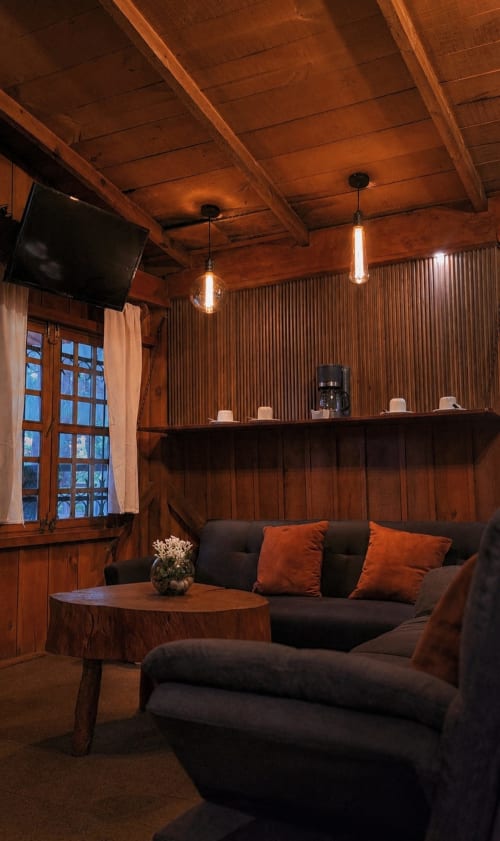 Rustic cabin lounge at Cabañas el Encanto with wooden beams, black sofa, pendant lights, and corrugated metal walls.