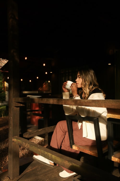 Woman enjoying warm beverage at night by wooden railing at Cabañas el Encanto, Las Vigas de Ramírez, with garden lights