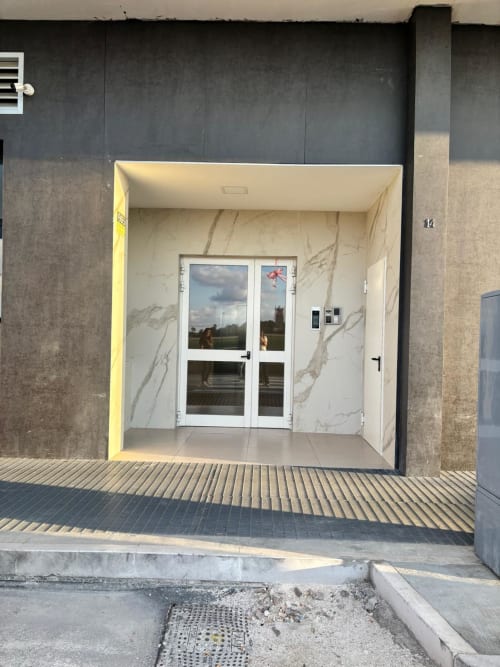 Ingresso moderno dell'appartamento Newhouse all'aeroporto di Bari con pareti in marmo e doppie porte in vetro