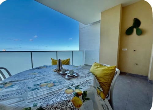 Balcone dell'appartamento dell'aeroporto di Bari con vista mare, tavolo da pranzo, cuscini gialli e orizzonte costiero