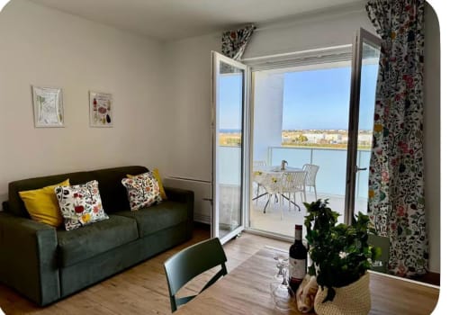 Elegante soggiorno con vista mare dal balcone dell'appartamento all'aeroporto di Bari, divano verde con cuscini floreali