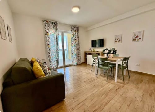 Moderno soggiorno a Bari con divano in oliva, tavolo da pranzo, TV e accesso al balcone con vista mare