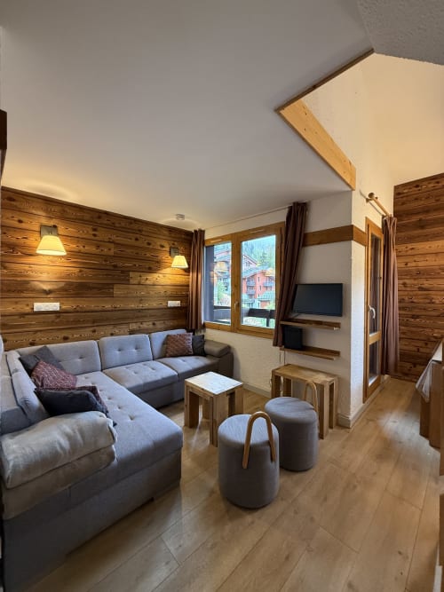 Salon d'appartement alpin moderne avec poutres apparentes, canapé gris en L et vue montagne à La Plagne