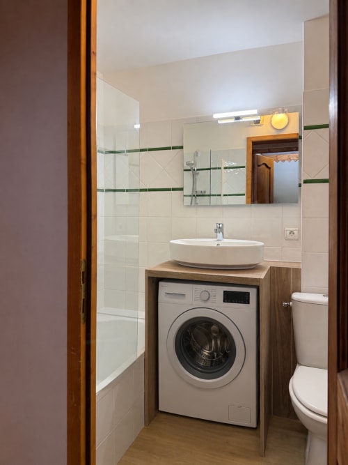 Salle de bain moderne avec lave-linge sous l'évier, appartement La Plagne Ski Confort, vasque blanche, miroir et vitrerie
