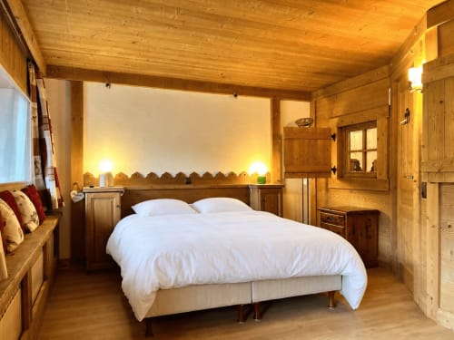 Chambre de chalet en bois à La Plagne avec literie blanche, poutres apparentes, vue montagne et décor alpin rustique