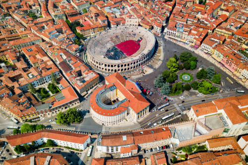 Vista aerea dell'Arena di Verona con tetto rosso, circondata da edifici storici in terracotta e spazi verdi