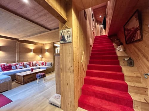 Entrée luxueuse du chalet alpin à La Plagne avec escalier en tapis rouge et salon intérieur en bois