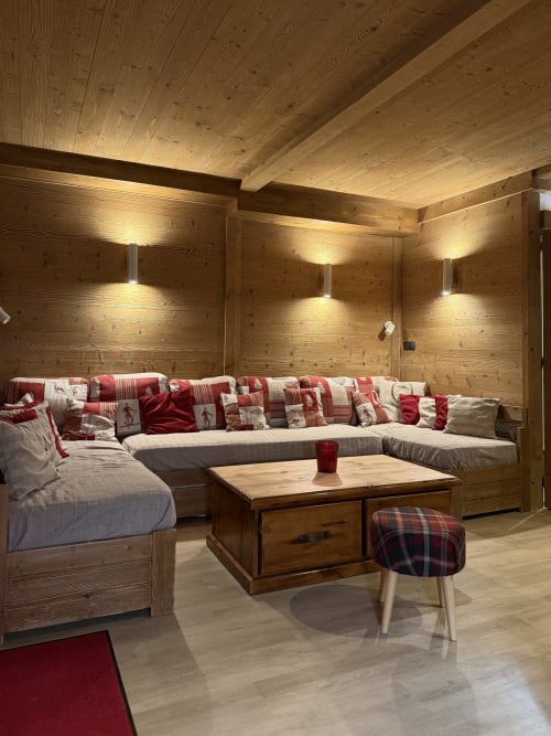 Salon douillet du chalet en bois à La Plagne avec sièges écossais rouges, cheminée et vue sur les montagnes