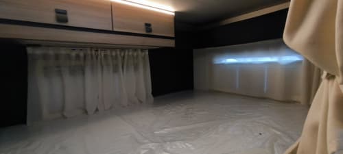 Interior de autocaravana Gozamena en Corralejo con cortinas blancas, iluminación moderna y protección de suelo