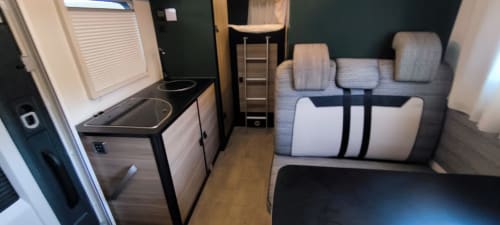 Interior de caravana Gozamena en Corralejo: cocina compacta, asientos tapizados grises, suelo de madera