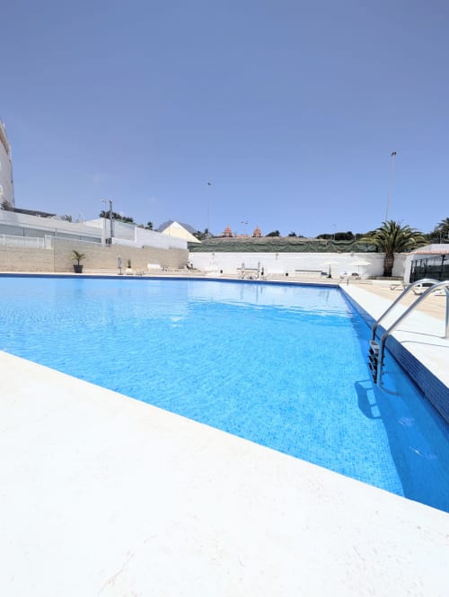 Bright blue Olympic-sized swimming pool at Manage Home Tenerife in Costa Adeje with white deck and palm trees