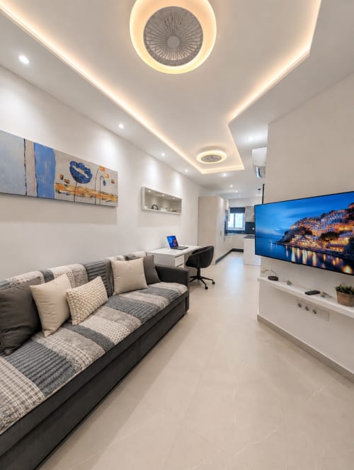 Modern apartment living room in Costa Adeje with gray sofa, wall-mounted TV, desk, and ceiling fan with warm lighting
