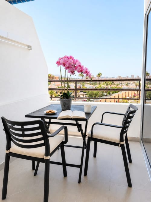 Balcony seating area at Manage Home Tenerife with pink orchids, black chairs, and Costa Adeje sea views