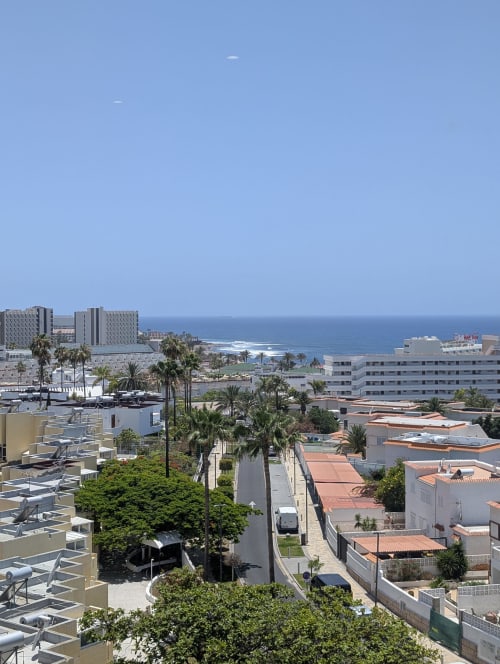 Coastal view of Costa Adeje apartment complex with terracotta roofs, palm trees, and Atlantic Ocean horizon in Tenerife