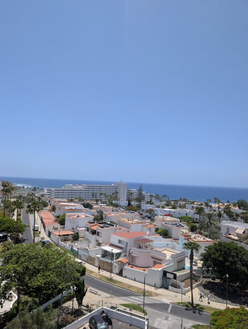 Coastal view of Costa Adeje apartment complex with Mediterranean buildings, palm trees, and blue ocean horizon