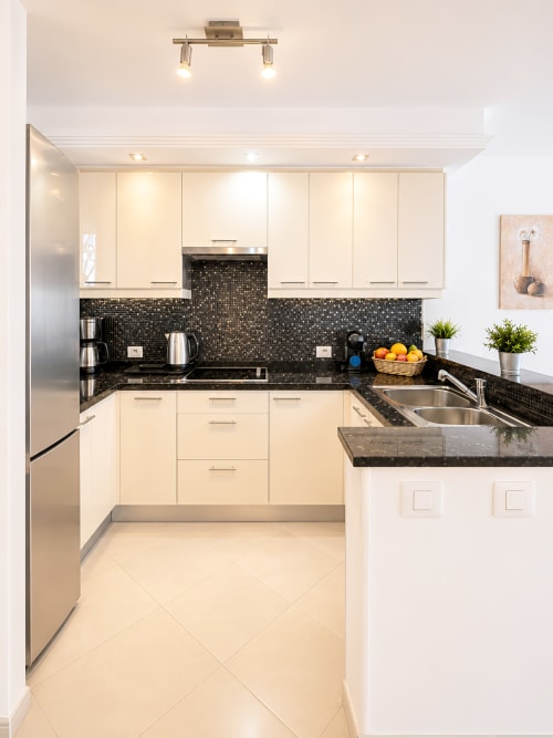 Modern kitchen with cream cabinets, black granite counters, and mosaic backsplash in Tenerife apartment