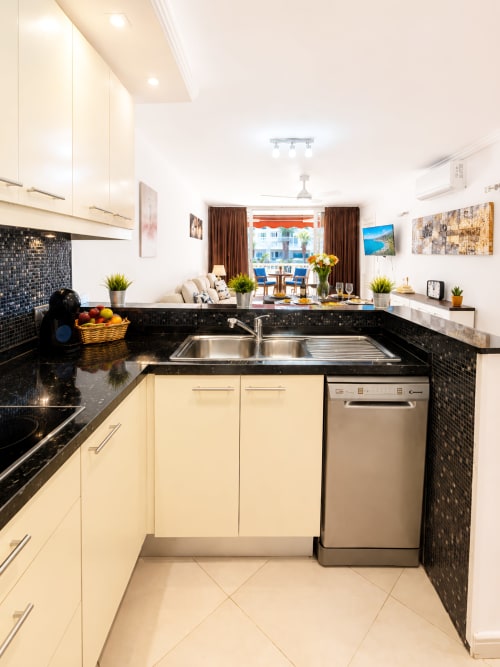 Modern kitchen with cream cabinets, black granite counters, and stainless steel appliances in Tenerife apartment