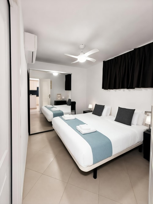 Modern twin bedroom in Playa de las Américas apartment with white beds, black accents, ceiling fan, and contemporary