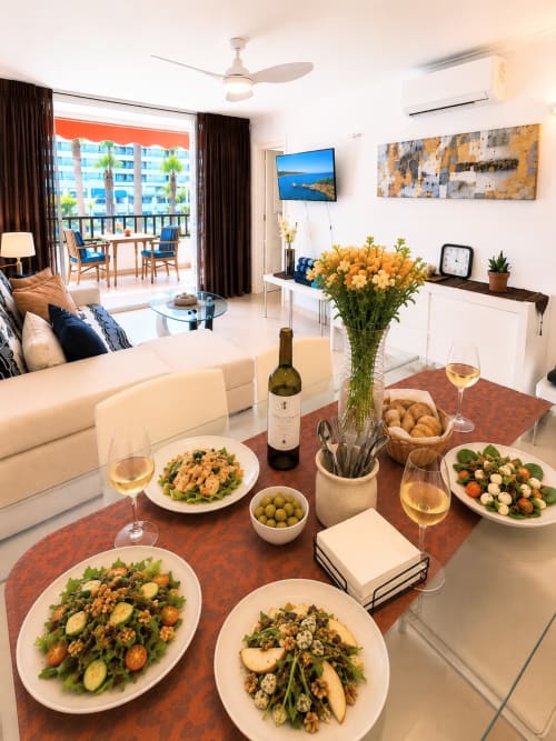 Elegant dining setup in Tenerife apartment with salads, wine, and ocean-view balcony overlooking Playa de las Américas