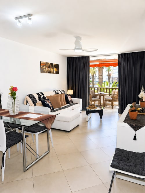 Modern apartment living room in Playa de las Américas with white sofa, dining area, ceiling fan, and ocean view balcony