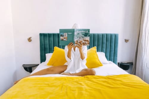 Chambre lumineuse du Boutique Hôtel Provencia Marseille avec parure jaune, tête de lit verte et guides touristiques de Marseille