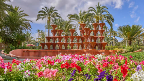 Jardín floral colorido con fuente de terracota roja en Alojamientos Boutique Velarde en Elche, rodeado de palmeras