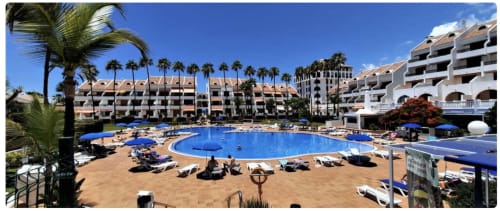 Resort pool area in Playa de las Américas, Tenerife with blue water, lounge chairs, palm trees and apartment buildings