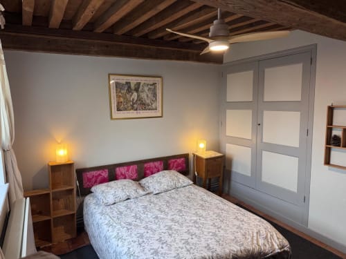 Chambre cosy au Gîte La Maison du Petit Louis avec lit queen, tête de lit en velours rose, poutres apparentes, tables de nuit avec lampes