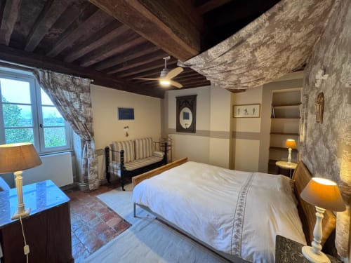 Chambre rustique aux Gîtes Changy Tourny avec poutres apparentes, lit blanc, banc rayé, murs en pierre, vue sur jardin